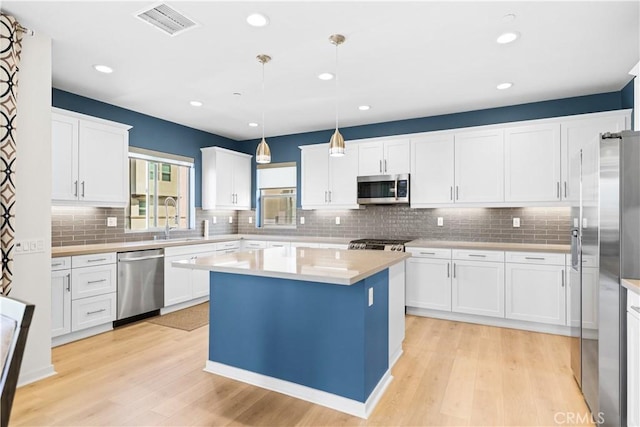 kitchen featuring sink, white cabinetry, hanging light fixtures, stainless steel appliances, and a center island