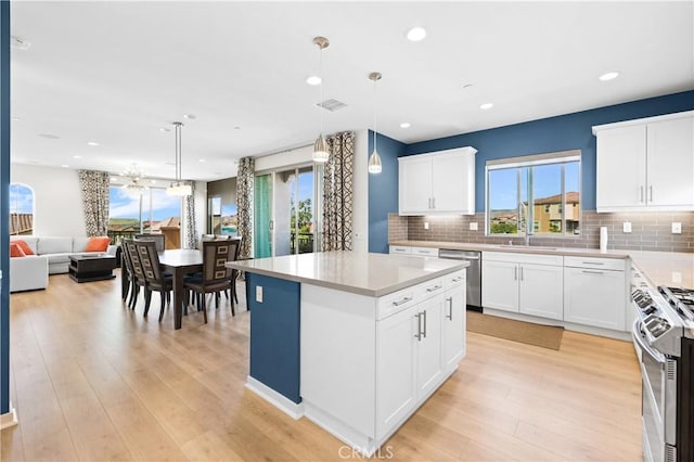 kitchen with a kitchen island, appliances with stainless steel finishes, decorative light fixtures, sink, and white cabinets