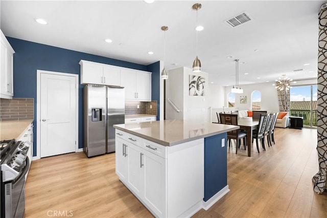 kitchen featuring white cabinetry, decorative light fixtures, appliances with stainless steel finishes, a kitchen island, and light hardwood / wood-style floors