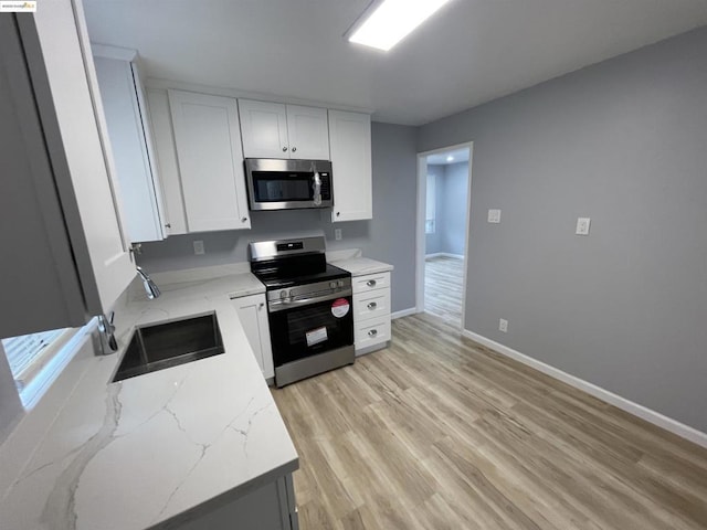 kitchen with white cabinetry, light stone countertops, stainless steel appliances, and sink