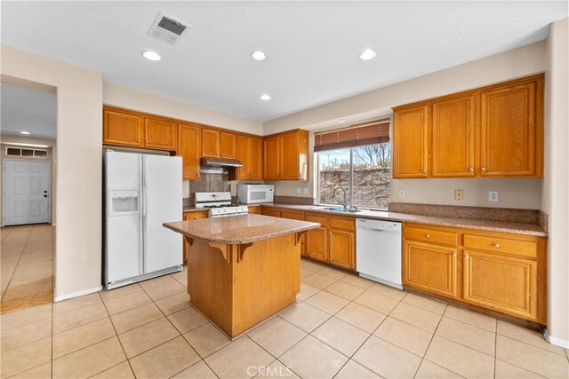 kitchen featuring visible vents, white appliances, a center island, under cabinet range hood, and a sink