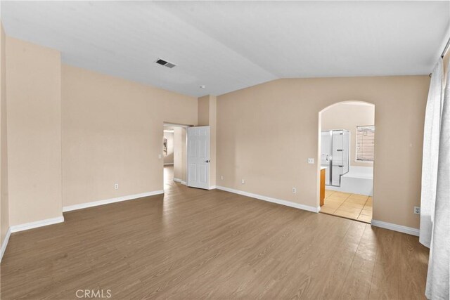 interior space featuring visible vents, arched walkways, baseboards, wood finished floors, and vaulted ceiling