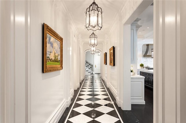 corridor with ornamental molding and an inviting chandelier