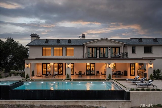 back house at dusk featuring pool water feature, a balcony, a swimming pool with hot tub, and a patio area