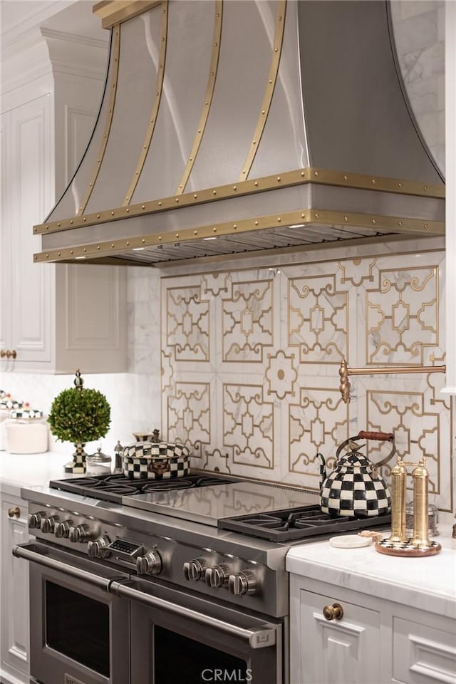 kitchen featuring double oven range, decorative backsplash, white cabinets, and premium range hood