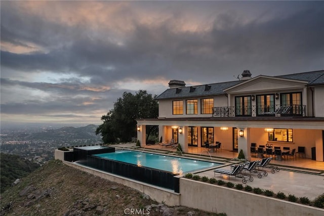 back house at dusk featuring a patio, a balcony, and pool water feature