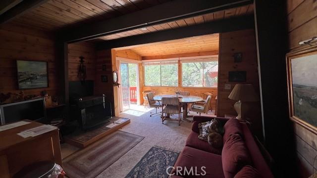 carpeted living room with wood ceiling, wooden walls, and vaulted ceiling with beams