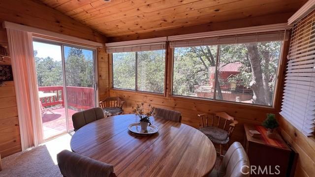 dining room featuring lofted ceiling, wooden walls, carpet floors, and wooden ceiling