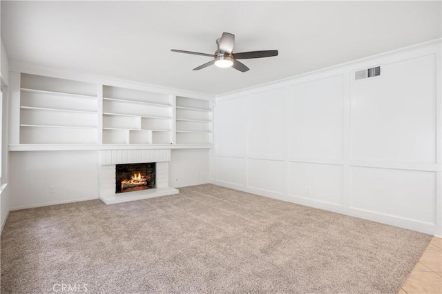 unfurnished living room with a fireplace, built in features, light colored carpet, and ceiling fan