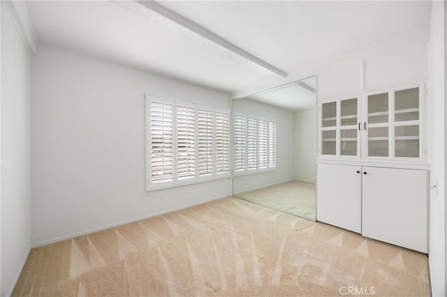 unfurnished bedroom with light colored carpet and beam ceiling