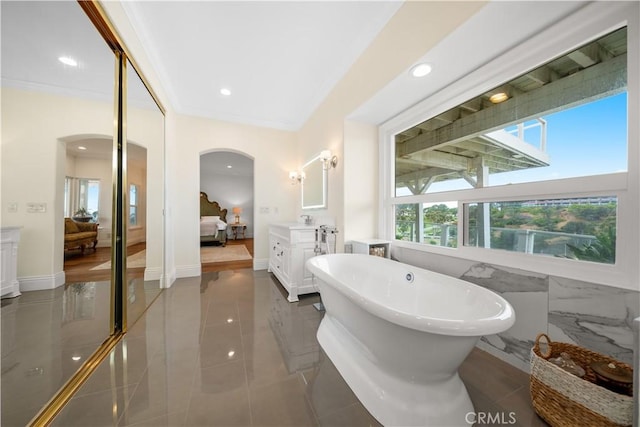 bathroom featuring baseboards, a soaking tub, ornamental molding, ensuite bathroom, and recessed lighting