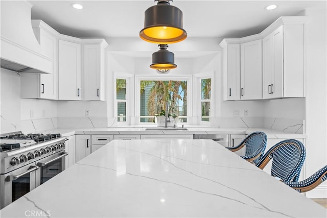 kitchen with stainless steel appliances, a sink, white cabinetry, decorative light fixtures, and custom range hood