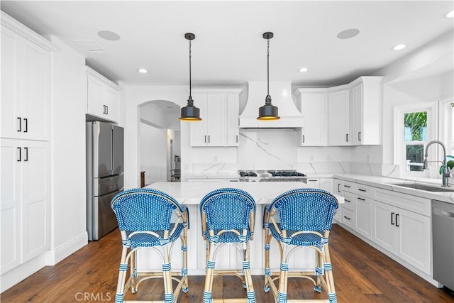 kitchen with appliances with stainless steel finishes, white cabinets, a sink, and hanging light fixtures