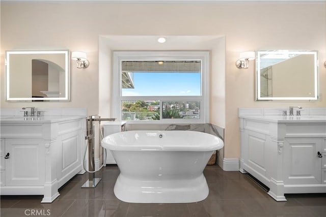 bathroom featuring a freestanding tub, two vanities, a sink, and tile patterned floors