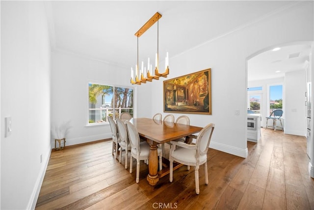 dining area featuring arched walkways, a notable chandelier, crown molding, and wood finished floors