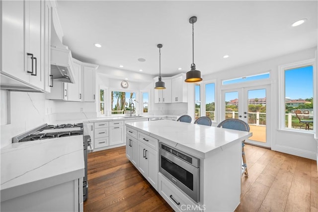 kitchen with a center island, a breakfast bar area, stainless steel appliances, white cabinetry, and light stone countertops