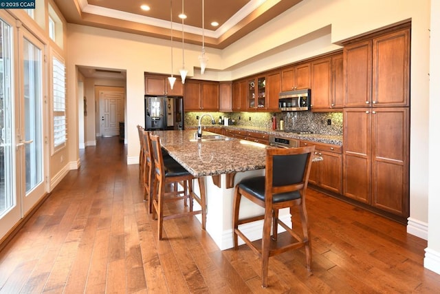 kitchen featuring black fridge with ice dispenser, sink, stone counters, pendant lighting, and a kitchen island with sink