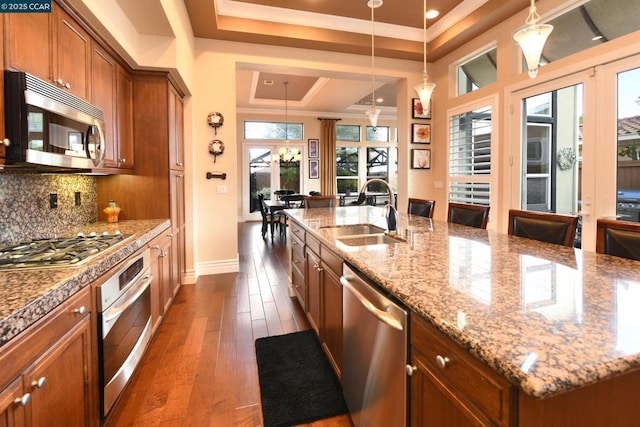 kitchen featuring sink, hanging light fixtures, a center island with sink, a raised ceiling, and stainless steel appliances