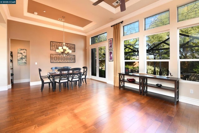 dining area with crown molding, a high ceiling, a tray ceiling, dark hardwood / wood-style flooring, and ceiling fan with notable chandelier