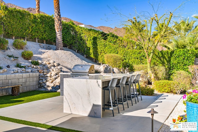 view of patio / terrace featuring an outdoor kitchen, exterior bar, a mountain view, and area for grilling