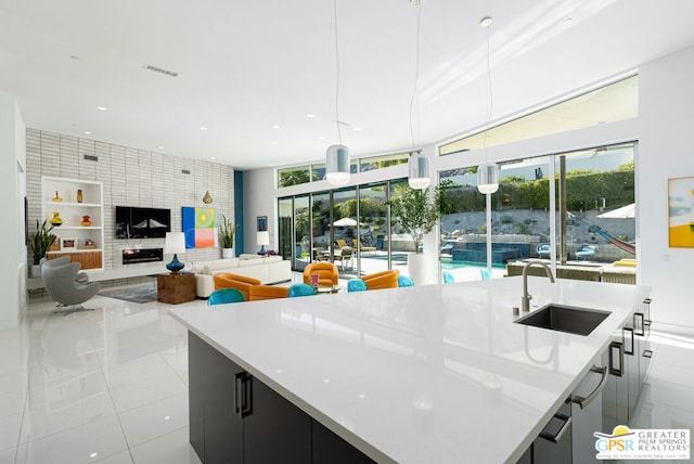 kitchen with sink, hanging light fixtures, a large fireplace, built in shelves, and a large island with sink