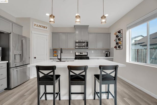 kitchen with gray cabinets, decorative light fixtures, an island with sink, sink, and stainless steel appliances