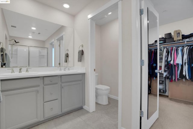 bathroom with a shower with door, vanity, tile patterned floors, and toilet