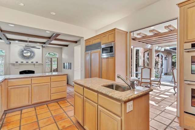 kitchen featuring an island with sink, sink, built in appliances, and light brown cabinetry