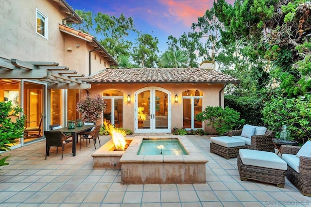 pool at dusk with a patio, an outdoor living space with a fire pit, and french doors