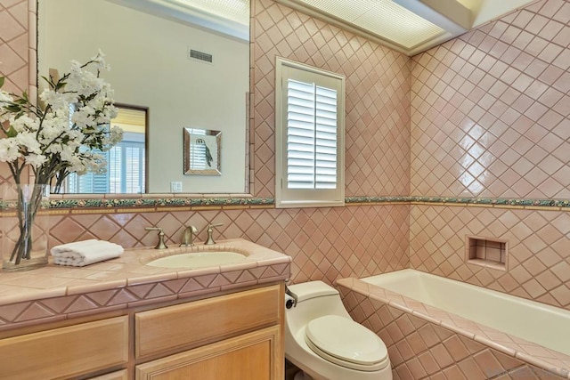 bathroom featuring vanity, toilet, tiled bath, and tile walls