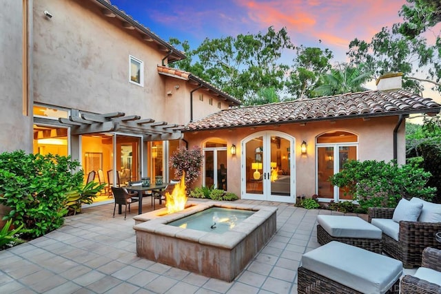 back house at dusk with french doors, a pergola, a patio, and an outdoor living space with a fire pit