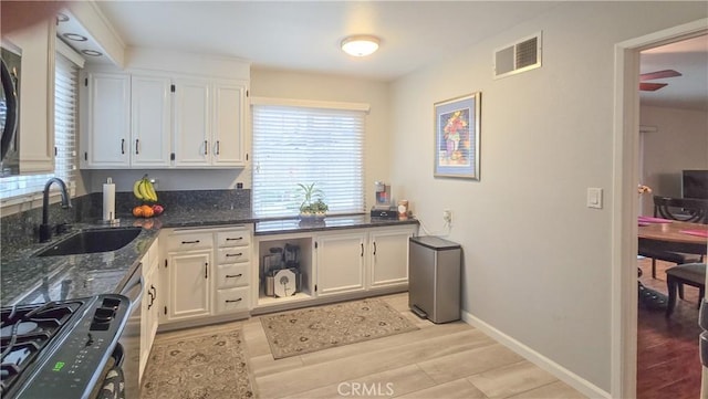 kitchen featuring black stove, sink, dark stone countertops, white cabinets, and light hardwood / wood-style flooring