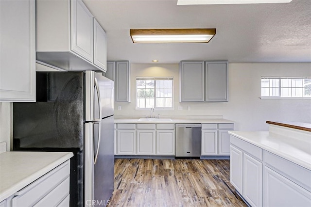 kitchen featuring sink, appliances with stainless steel finishes, white cabinetry, hardwood / wood-style floors, and a textured ceiling