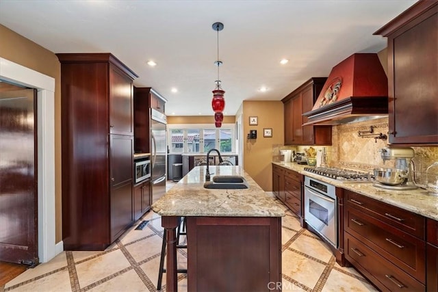 kitchen with premium range hood, sink, decorative light fixtures, a center island with sink, and stainless steel appliances