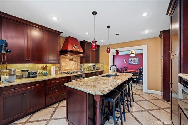 kitchen featuring decorative light fixtures, sink, backsplash, custom exhaust hood, and a kitchen island with sink