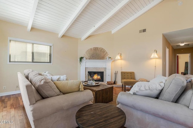 living room with a tile fireplace, vaulted ceiling with beams, and hardwood / wood-style floors