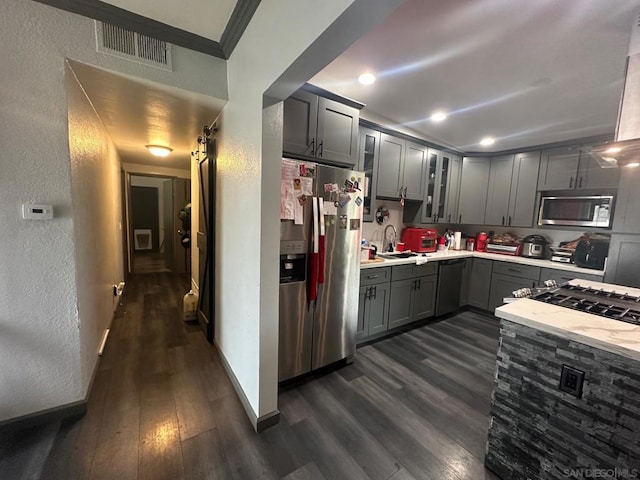 kitchen featuring stainless steel appliances, ornamental molding, gray cabinetry, and dark hardwood / wood-style flooring