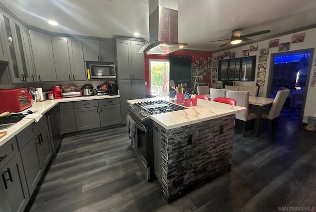 kitchen with gray cabinets, ceiling fan, appliances with stainless steel finishes, dark hardwood / wood-style floors, and island exhaust hood