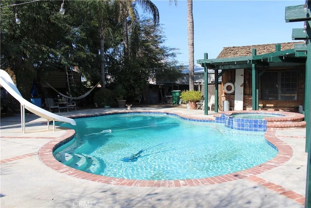 view of pool with a water slide, a patio area, and an in ground hot tub