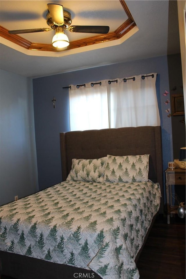 bedroom with a raised ceiling, dark hardwood / wood-style flooring, and ceiling fan