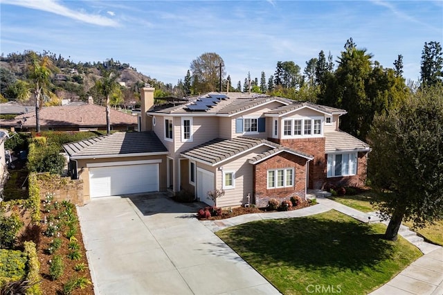 traditional-style house with concrete driveway, a tile roof, an attached garage, roof mounted solar panels, and brick siding