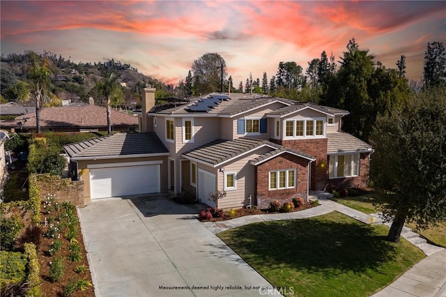 view of front facade featuring a tile roof, brick siding, an attached garage, roof mounted solar panels, and driveway