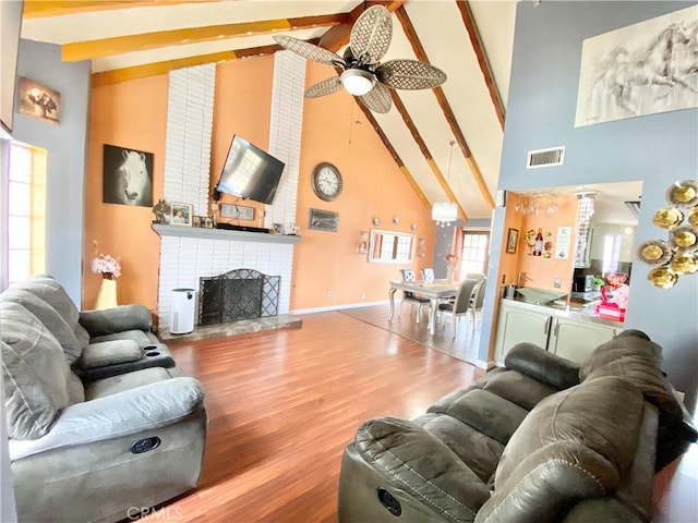 living room with hardwood / wood-style flooring, ceiling fan, beam ceiling, high vaulted ceiling, and a fireplace