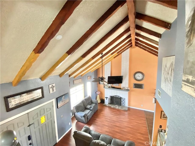 living room featuring wood-type flooring, a tile fireplace, lofted ceiling with beams, and ceiling fan