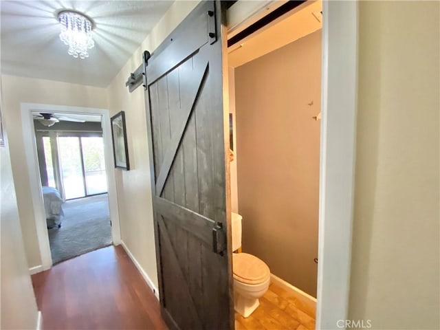 corridor with a barn door, baseboards, and dark wood finished floors