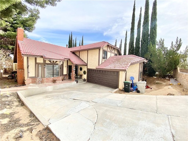 tudor house with a garage, a tiled roof, concrete driveway, stucco siding, and a chimney