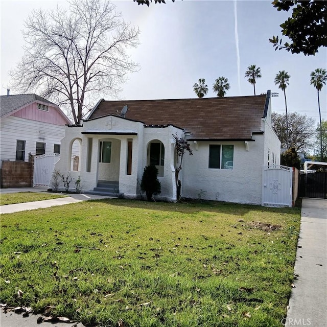 bungalow-style house with stucco siding, roof with shingles, fence, and a front yard