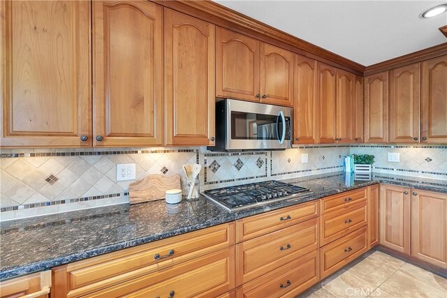 31750 1st St, Acton, CA 93510 - kitchen with stainless steel appliances, dark stone countertops, backsplash, brown cabinets, and light tile patterned floors