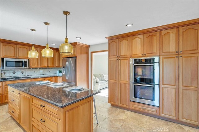 31750 1st St, Acton, CA 93510 - kitchen featuring dark stone countertops, backsplash, a center island, appliances with stainless steel finishes, and a breakfast bar area