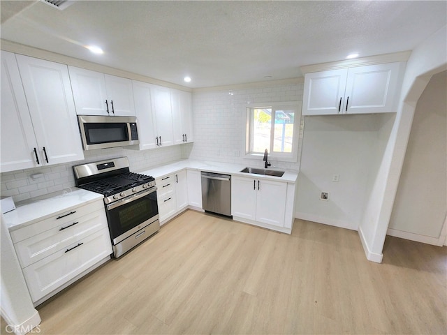 kitchen featuring sink, light hardwood / wood-style flooring, appliances with stainless steel finishes, white cabinetry, and decorative backsplash